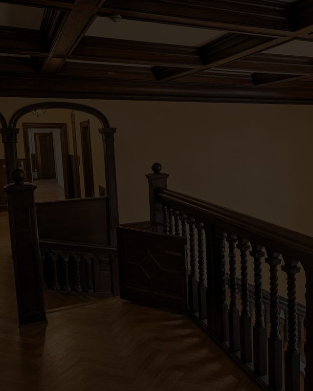 A first-floor landing with a carved balustrade and an arch onto a lit corridor