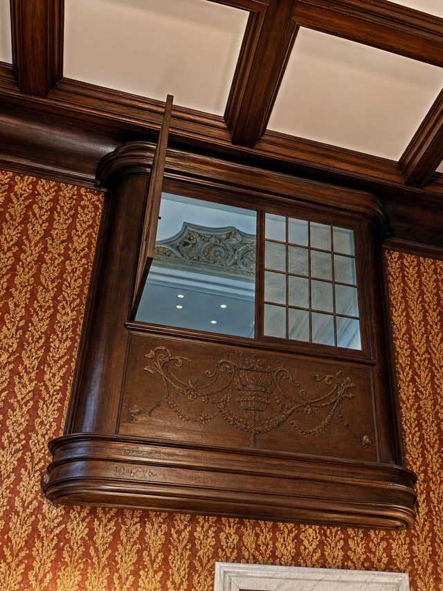 The carved apron of a timber oriel bay under a coffered ceiling