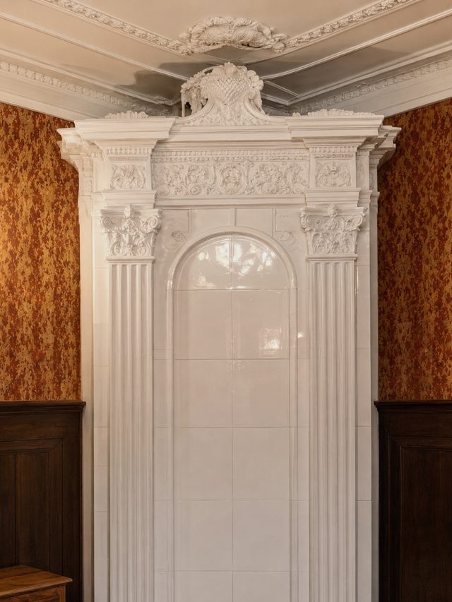 The fluted pilasters and carved crown of a white glazed stove portal