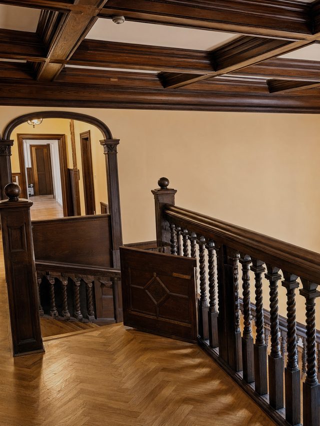 A round arch on a carved oak pier, a corridor beyond it and a door standing open at the end, over herringbone parquet