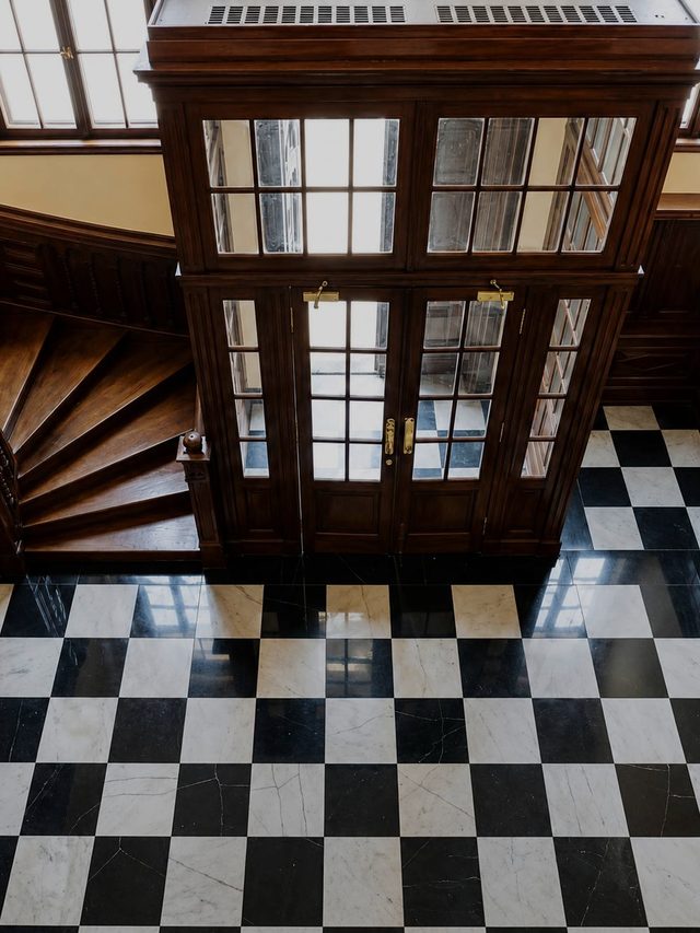 A chequered black and white marble floor seen from above, beside the glazed timber enclosure of the stair