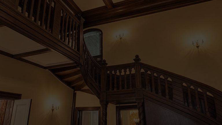 A dark stair hall lit only by three wall sconces, the carved balustrade turning above and a lamp burning in a room through an open door